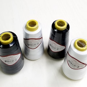 May include: Four large spools of Cotton Valley sewing thread, two in black and two in white, each wrapped in clear plastic with a yellow top cap. Each spool features a label with the text SEWING THREAD, 100% POLYESTER, and a barcode.