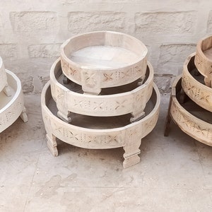 May include: Three sets of decorative wooden serving trays in varying sizes. The trays are round with carved floral designs and are stacked in sets of three. One set is painted white, and the others are natural wood tones.