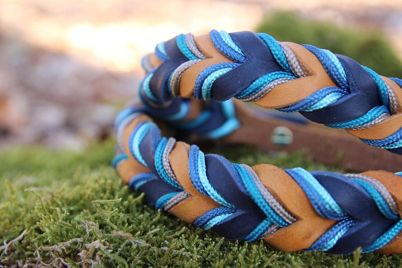 May include: A braided leather dog collar with blue, grey, and brown accents. The collar is braided with a rope-like texture.