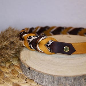 May include: A braided belt featuring alternating strands of tan leather, dark brown leather, and a fabric strip with a black and white leopard print pattern. The belt includes a gold-toned metal rivet and a series of holes for adjustment.