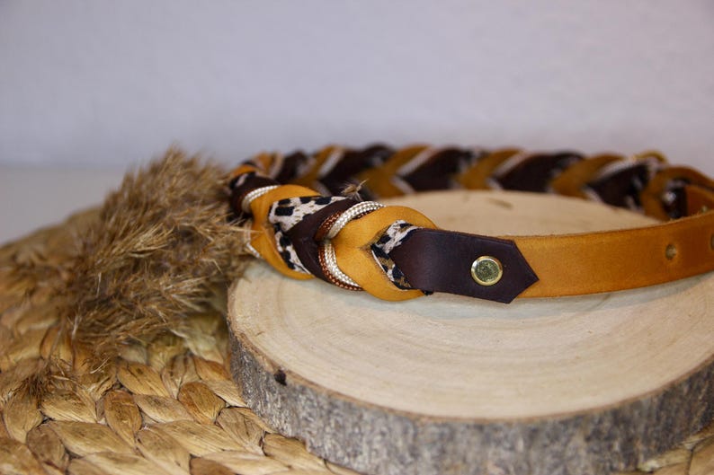 May include: A braided belt featuring alternating strands of tan leather, dark brown leather, and a fabric strip with a black and white leopard print pattern. The belt includes a gold-toned metal rivet and a series of holes for adjustment.
