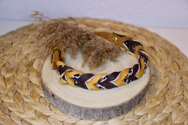 May include: A braided pet collar featuring alternating strands of mustard yellow, dark brown, and a black and white patterned fabric. The collar includes a gold-toned metal D-ring and a matching gold-toned metal stud fastener for secure closure.