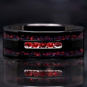 May include: A black ring with a rectangular design. The ring features a row of five red gemstones and is accented with red and purple stones. The ring is reflected in the surface below.