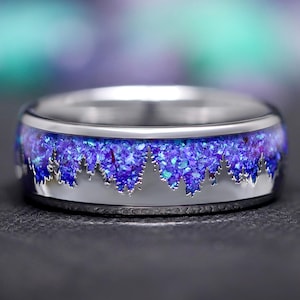 Könnte beinhalten: Ein silberner Ring mit einem glitzernden Inlay in Lila und Blau. Der Glitter ist in einem unregelmäßigen Muster um das Band des Rings angeordnet.