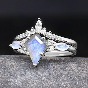 May include: A silver ring set with a large, faceted, iridescent blue gemstone. The ring is accented with smaller clear gemstones and two smaller, oval, iridescent blue gemstones.