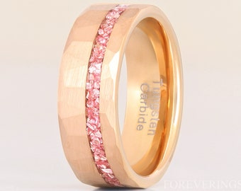 May include: A rose gold tungsten carbide ring with a faceted exterior and a central band filled with pink gemstones. The ring has the text "Tungsten Carbide" engraved on the inside.