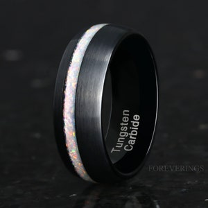 Peut inclure: Bague en carbure de tungstène noire avec une incrustation d'opale blanche et les mots "Tungsten Carbide" gravés sur le côté.