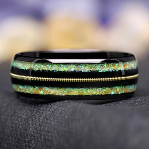 May include: A black tungsten carbide ring with two thin gold bands and green opal inlay.