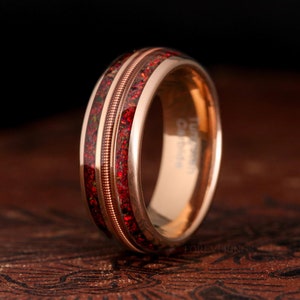 May include: A rose gold tungsten carbide ring with a red and gold inlay. The ring has a polished finish and a comfortable fit.