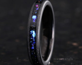 May include: Black tungsten carbide ring featuring a thin blue and silver inlay. The inlay has a sparkly, galaxy-like appearance.