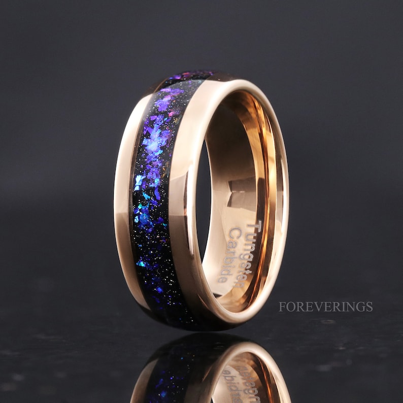 Puede incluir: Un anillo de carburo de tungsteno de oro rosa con una incrustaci&oacute;n de purpurina negra y azul. El anillo est&aacute; grabado con "Tungsten Carbide Canada".