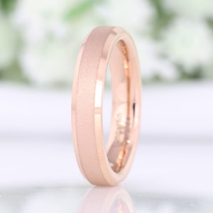May include: A rose gold wedding band with a brushed finish. The band has a beveled edge and a slightly rounded profile.