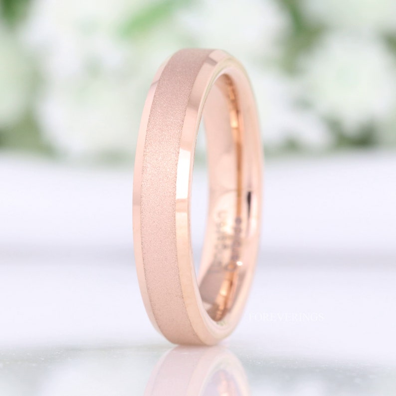 May include: A rose gold wedding band with a brushed finish. The band has a beveled edge and a slightly rounded profile.