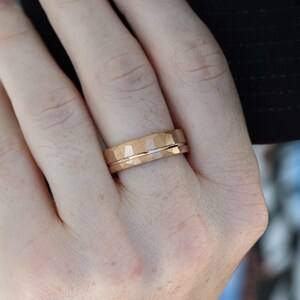 May include: A rose gold wedding band with a hammered finish and a polished center band.
