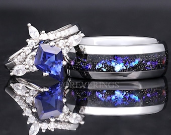 Puede incluir: Un par de anillos de boda con un anillo de compromiso de zafiro azul. El anillo de compromiso presenta un zafiro grande de talla cojín rodeado de diamantes más pequeños. La banda de boda es una banda plateada con un diseño de galaxia negro y azul.