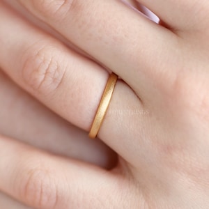May include: A simple gold band ring worn on a finger. The ring is smooth and has a matte finish.