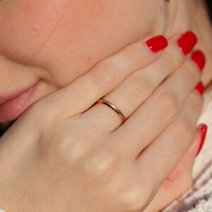 May include: A thin rose gold band ring with a polished finish. The ring is worn on the ring finger of a person's left hand.