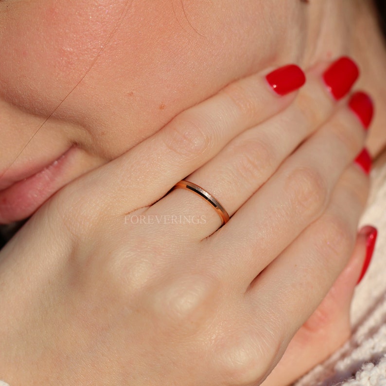 May include: A thin rose gold band ring with a polished finish. The ring is worn on the ring finger of a person's left hand.