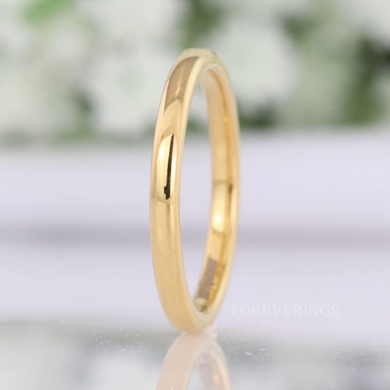 Thin 2mm gold tungsten wedding band standing upright, polished dome catching the light