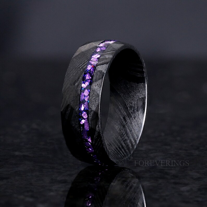 May include: A black carbon fiber ring with a purple glitter inlay. The ring is a simple band with a smooth finish.