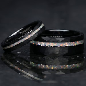 May include: Two black tungsten carbide rings with a hammered finish and a thin opal inlay. The rings are stacked on top of each other.