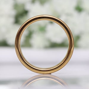 May include: A close-up shot of a gold-colored ring. The ring has a smooth, polished surface and a rounded band. The background is blurred, with white and green tones. The text "FOREVERRINGS" is visible on the ring.