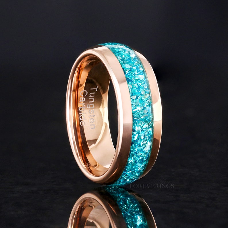 May include: A rose gold tungsten carbide ring with a turquoise inlay. The ring is engraved with the words "Tungsten Carbide".