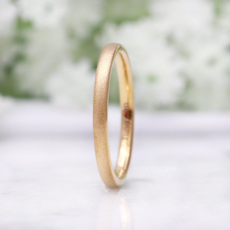 May include: A simple gold wedding band with a brushed finish. The band is thin and has a rounded edge.