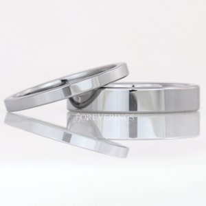 May include: Two silver wedding bands, one slightly wider than the other, are stacked on top of each other. The bands are polished and have a smooth, flat surface. The bands are reflected in the white surface below.