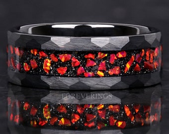 May include: A black ring with a hammered texture and a band of red and orange gemstones set in a black speckled background. The ring has a polished, reflective surface.
