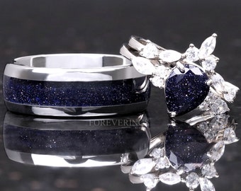 Può includere: Un set di due fedi nuziali con un designo a cielo stellato blu. La fede a sinistra è una semplice fede d'argento con un'intarsio a cielo stellato blu. La fede a destra è una fede d'argento con una grande pietra blu a forma di cuore circondata da pietre più piccole e chiare.