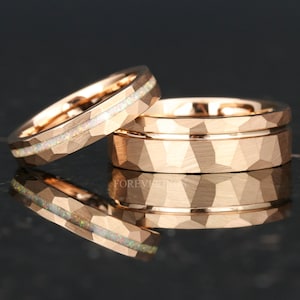 May include: Two rose gold wedding bands. One band has a hammered finish and a thin rose gold band around the center. The other band has a hammered finish and a thin white opal inlay.