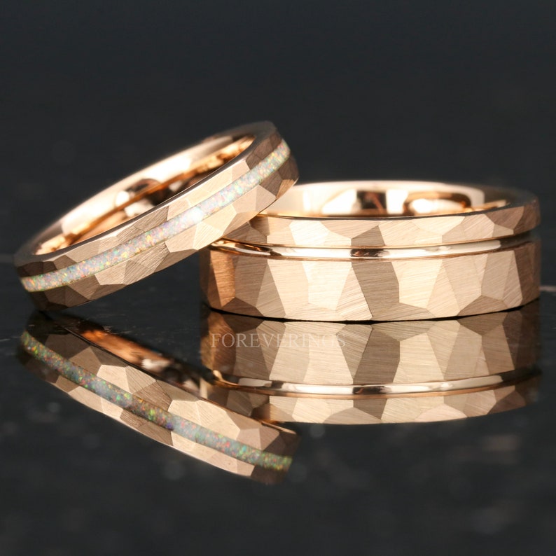 May include: Two rose gold wedding bands. One band has a hammered finish and a thin rose gold band around the center. The other band has a hammered finish and a thin white opal inlay.
