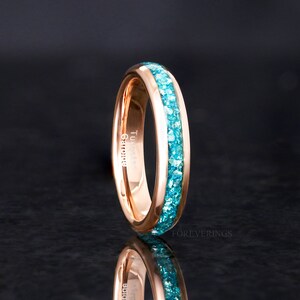 May include: Rose gold ring with a turquoise gemstone band. The ring is engraved with the words "Tungsten Carbide".