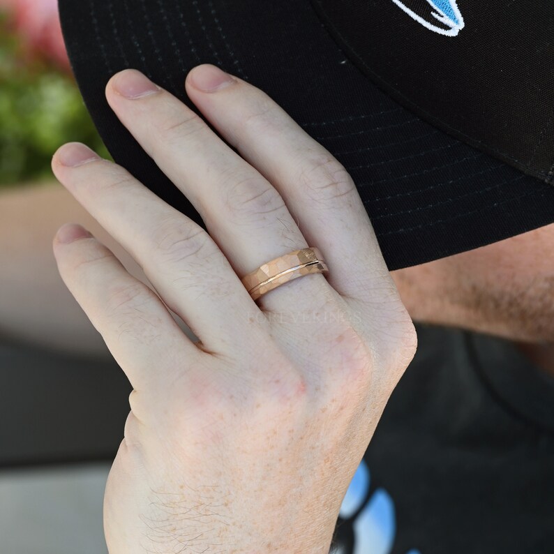 May include: A close-up of a person's hand wearing a rose gold hammered band ring.
