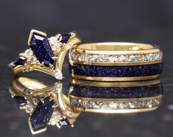 May include: A pair of gold wedding bands with a blue and white sparkle finish. The band on the left has a unique V-shaped design with a larger blue stone in the center. The band on the right has two rows of white stones.