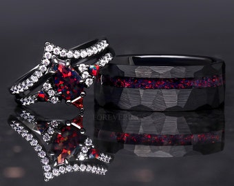 Könnte beinhalten: Ein schwarzer Wolframcarbid-Ring mit einer roten und schwarzen Opal-Einlage und ein schwarzer und weißer Diamantring mit einem roten Opal-Mittelstück. Die Ringe spiegeln sich auf einer schwarzen Oberfläche.