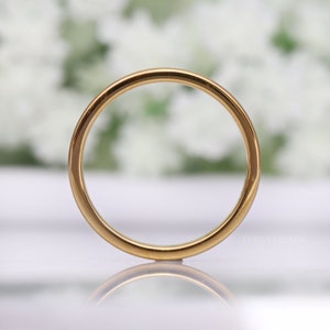 May include: A close-up shot of a gold-colored ring. The ring is circular and has a smooth, polished surface. The word "FOREVERRINGS" is visible on the ring. The background is blurred, with white and green tones.
