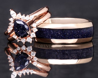 May include: A pair of rose gold wedding bands with a blue starry sky design. The engagement ring features a pear-shaped blue stone surrounded by smaller clear stones.