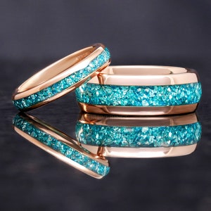 May include: Two rose gold wedding bands with a blue gemstone inlay. The bands are stacked on top of each other.