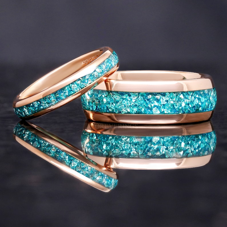 May include: Two rose gold wedding bands with a blue gemstone inlay. The bands are stacked on top of each other.