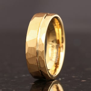 May include: A gold-colored ring with a textured, faceted surface. The ring has a central groove and a polished inner band. The word "FOREVERRINGS" is visible in the background.