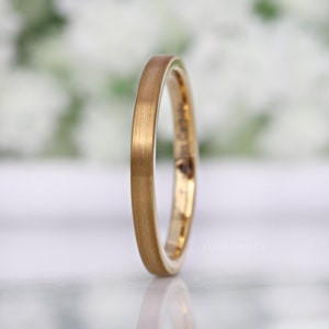 May include: A gold-colored ring with a brushed finish. The ring has a thin band and a smooth, matte texture. The word "FOREVERRINGS" is printed on the side of the ring. The ring is likely made of tungsten carbide.