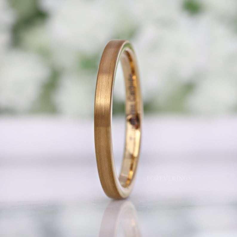 May include: A gold-colored ring with a brushed finish. The ring has a thin band and a smooth, matte texture. The word "FOREVERRINGS" is printed on the side of the ring. The ring is likely made of tungsten carbide.