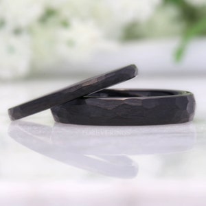 May include: Two black wedding bands with a hammered finish. The bands are stacked on top of each other.