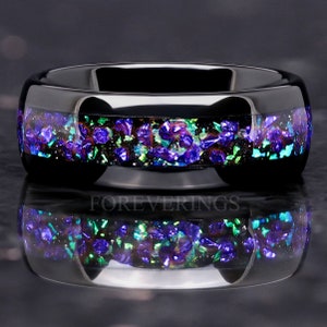 May include: A black ceramic ring with a band of iridescent purple, green, and silver glitter embedded in the surface. The ring is shown on a black background.