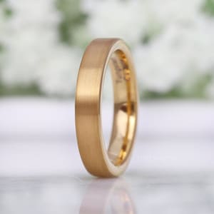 May include: A gold-colored ring with a brushed finish. The ring has a flat profile and a smooth, matte surface. The inside of the ring is a shiny gold color. The ring is likely made of tungsten. The word "Foreverings" is printed on the ring.