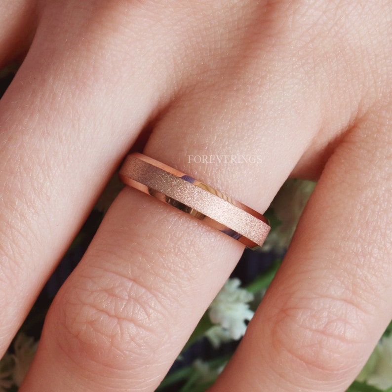May include: A rose gold wedding band with a brushed finish. The band is worn on a finger.