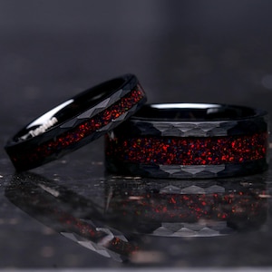 May include: Two black tungsten carbide rings with a red glitter inlay. The rings have a faceted, textured finish.