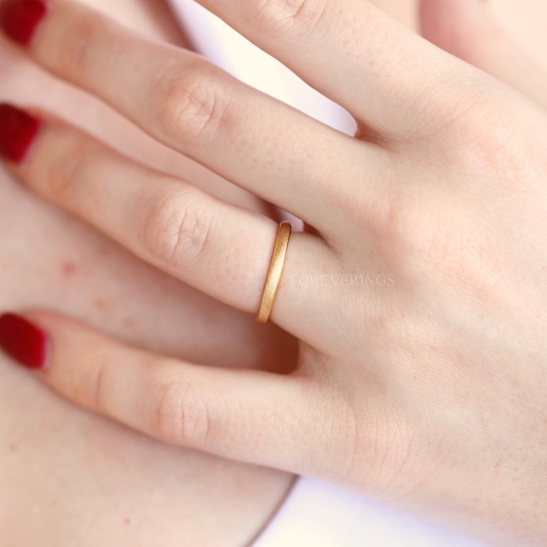 May include: A simple gold band ring worn on a finger. The ring is smooth and has a matte finish.